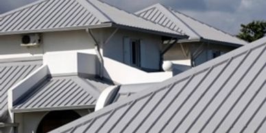 Modern white building with multiple gray metal roofs under a cloudy sky.