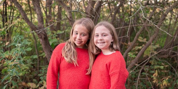 Two girls in matching red sweaters smile together outdoors.