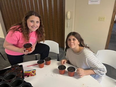 Two young women planting seeds in small pots indoors.