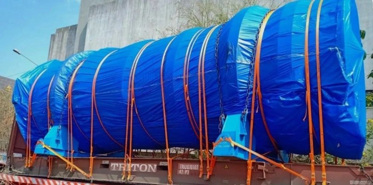 Large industrial equipment securely wrapped in blue tarpaulin and strapped on a flatbed trailer.
