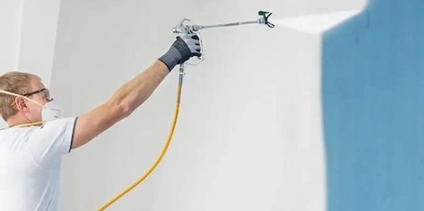 Decorator using airless spray gun to paint a white interior wall