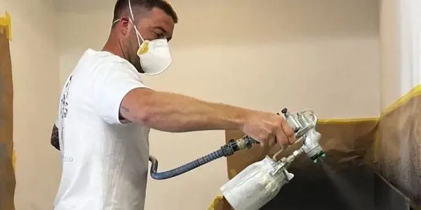 Painter using spray gun to respray a kitchen worktop and units