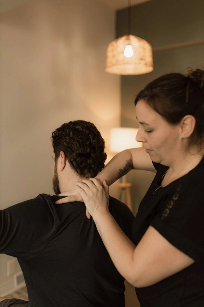 Therapist giving a neck massage to a seated man in a cozy room.