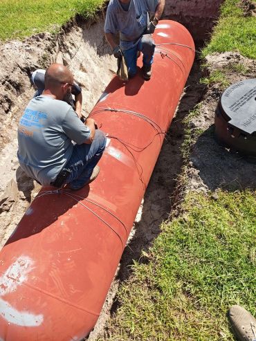 Two workers installing a large red pipe in a trench.