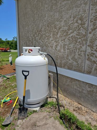 Large propane tank beside a textured wall with a shovel leaning on it.