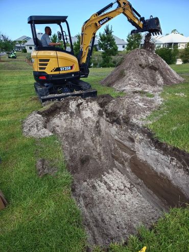 Excavator digs a trench in a grassy yard.