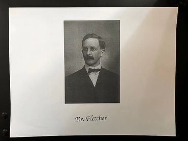 A male doctor with dark brown hair from the early 20th century.