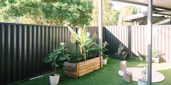 A backyard with artificial grass, potted plants, and a wooden planter box.