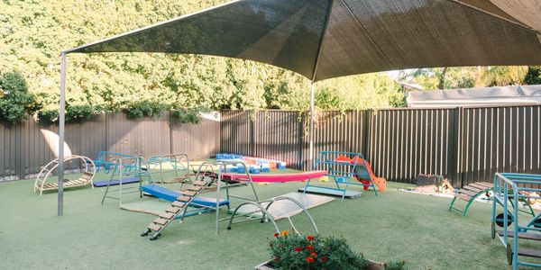 Outdoor playground with climbing frames and slides under a sunshade.