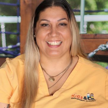 Smiling woman in yellow Kids & Co. Educational Academy shirt.