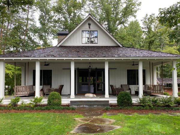 Cozy white house with a porch and chairs surrounded by trees.