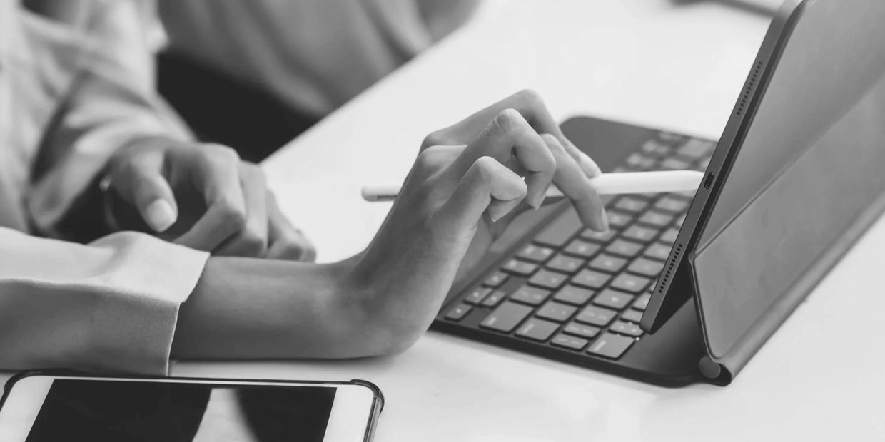 Woman sitting at a desk holding a stylus and writing on the screen of an e-tablet.