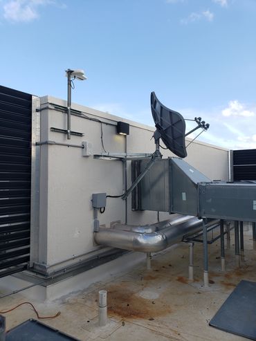 Satellite dish and ventilation system on a rooftop under a clear sky.