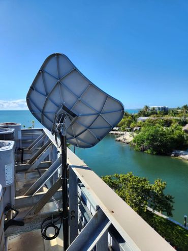 Satellite dish on a rooftop overlooking water and greenery under a clear sky.