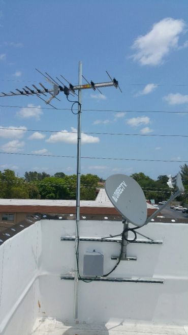 Rooftop with TV antenna and DIRECTV satellite dish under a partly cloudy sky.