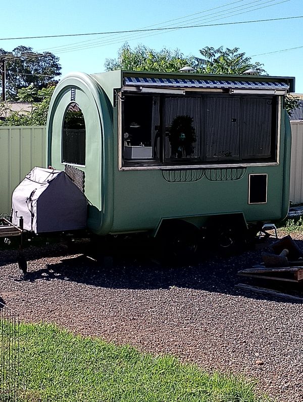Green vintage-style caravan parked on a gravel lot with a covered hitch.