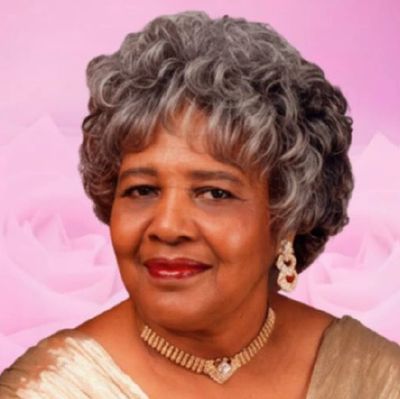 Elegant older woman with gray hair and a warm smile against a pink floral background.