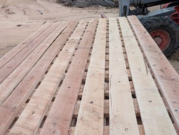 Stack of wooden planks outdoors near construction equipment.