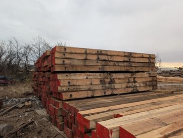 Stacked wooden railroad ties with red-painted ends in an outdoor storage area.