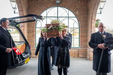 Mourners carrying a floral basket urn at a compassionate funeral service.
