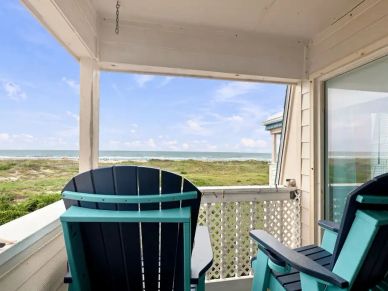 Two teal Adirondack chairs on a porch overlooking the ocean.