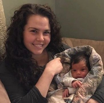 Woman smiling and holding a baby wrapped in a blanket.