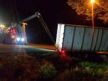 A tow truck pulls a stuck trailer from a ditch at night under a streetlight.