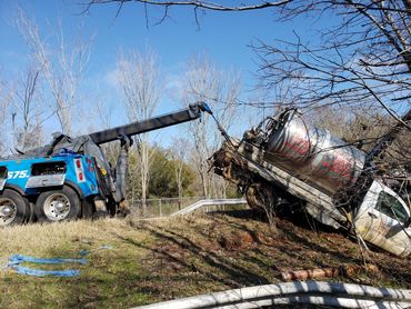 Tow truck recovering a tipped portable toilet rental truck from a grassy ditch.