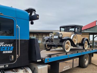 A vintage beige and black car on a blue and black wrecker truck in Athens, TX.