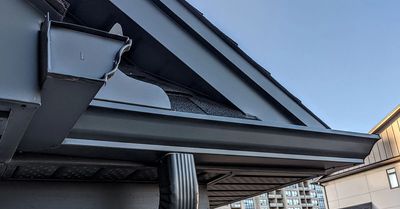 Close-up of a black metal gutter and downspout on a house roof.