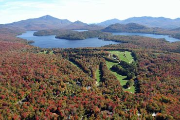 Aerial view of a forest with colorful autumn foliage and a golf course by a lake.