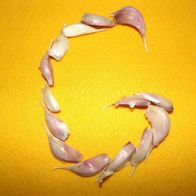 Garlic cloves arranged to form the letter G on a yellow background.