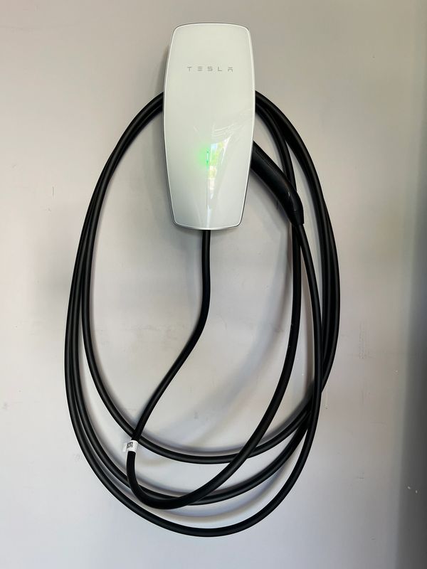Wall-mounted Tesla electric vehicle charger with coiled cable.