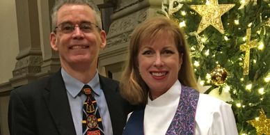 Smiling couple dressed formally in front of a decorated Christmas tree.