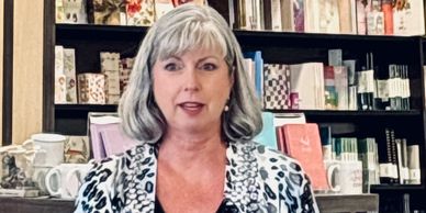 A woman with gray hair in a patterned jacket stands in a shop.