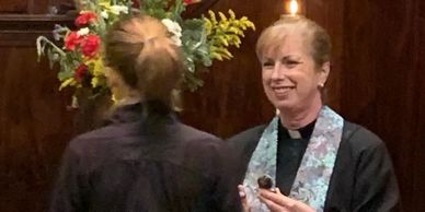 A smiling clergywoman holding a small object during a ceremony.