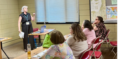 A woman presents to a small group seated in a classroom setting.