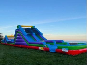 Colorful inflatable water slide set up on a grassy field under a clear blue sky.