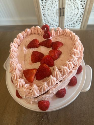Heart-shaped strawberry cake with pink frosting and a number 3 candle.