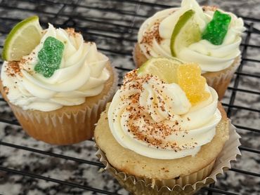 Cupcakes with creamy frosting, lime slices, and gummy bears on a cooling rack.