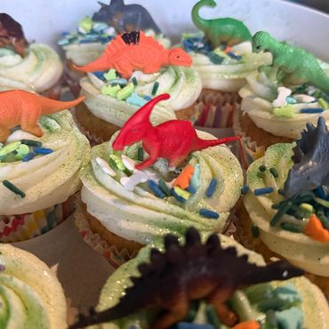 Cupcakes decorated with small colorful dinosaur toys and sprinkles.