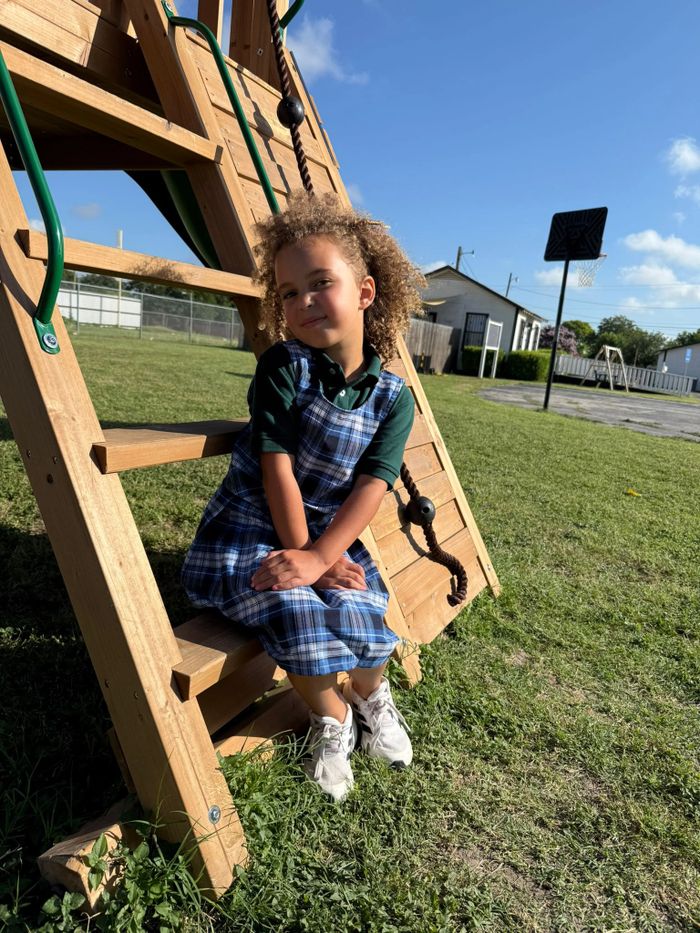 Young girl sitting on wooden playground steps on a sunny day.