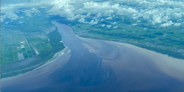 Aerial view of a river meeting the ocean under a cloudy sky.