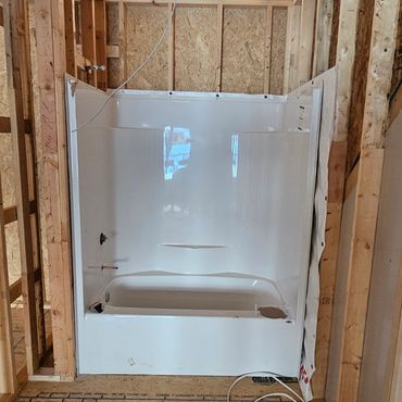 Bathtub installed in unfinished wooden frame bathroom under construction.