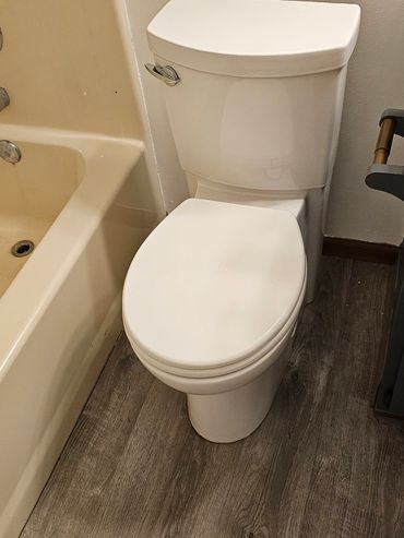 A white toilet next to a beige bathtub on wood-textured flooring.