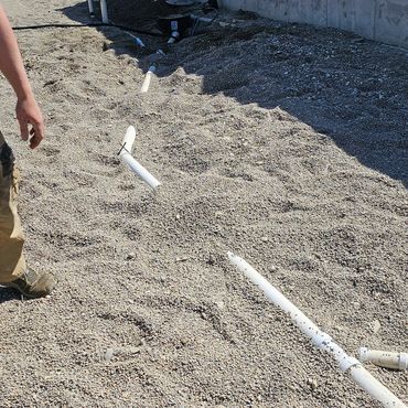 Construction site with visible plumbing pipes laid on gravel near concrete walls.