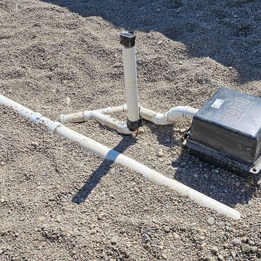 White PVC pipes and a black box on gravel in front of a concrete wall.