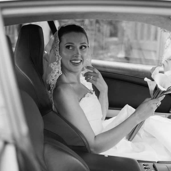 Bride in wedding dress sitting in car, smiling.