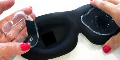 Hands holding parts of a black eye mask.