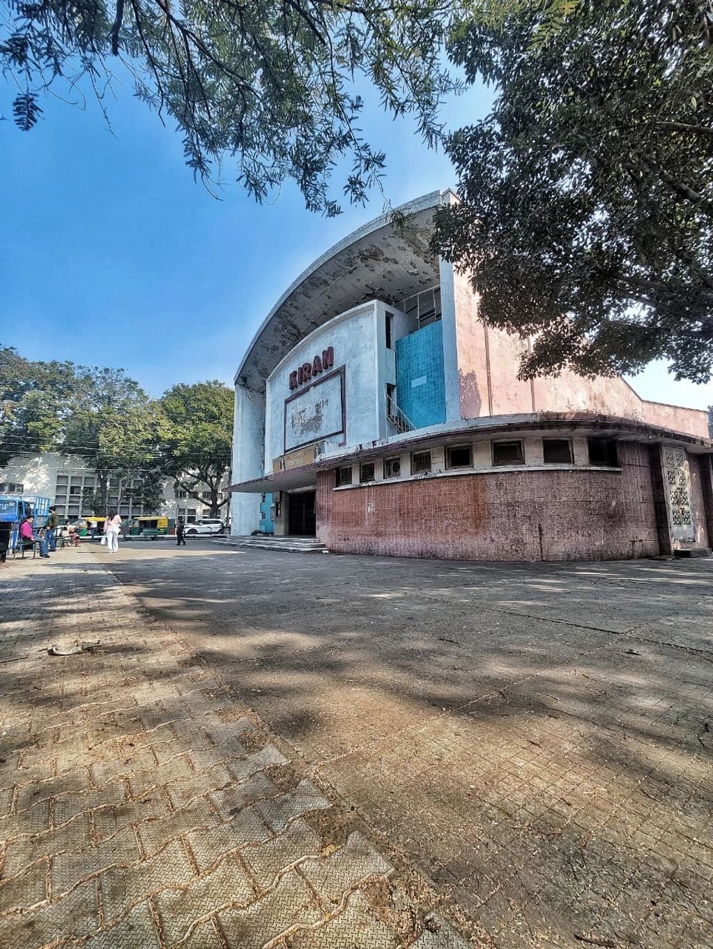 Old cinema building with 'KIRAN' signage under trees.